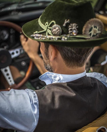 Traditional German Oktoberfest hat with feather and pins resting on a wooden beer table.