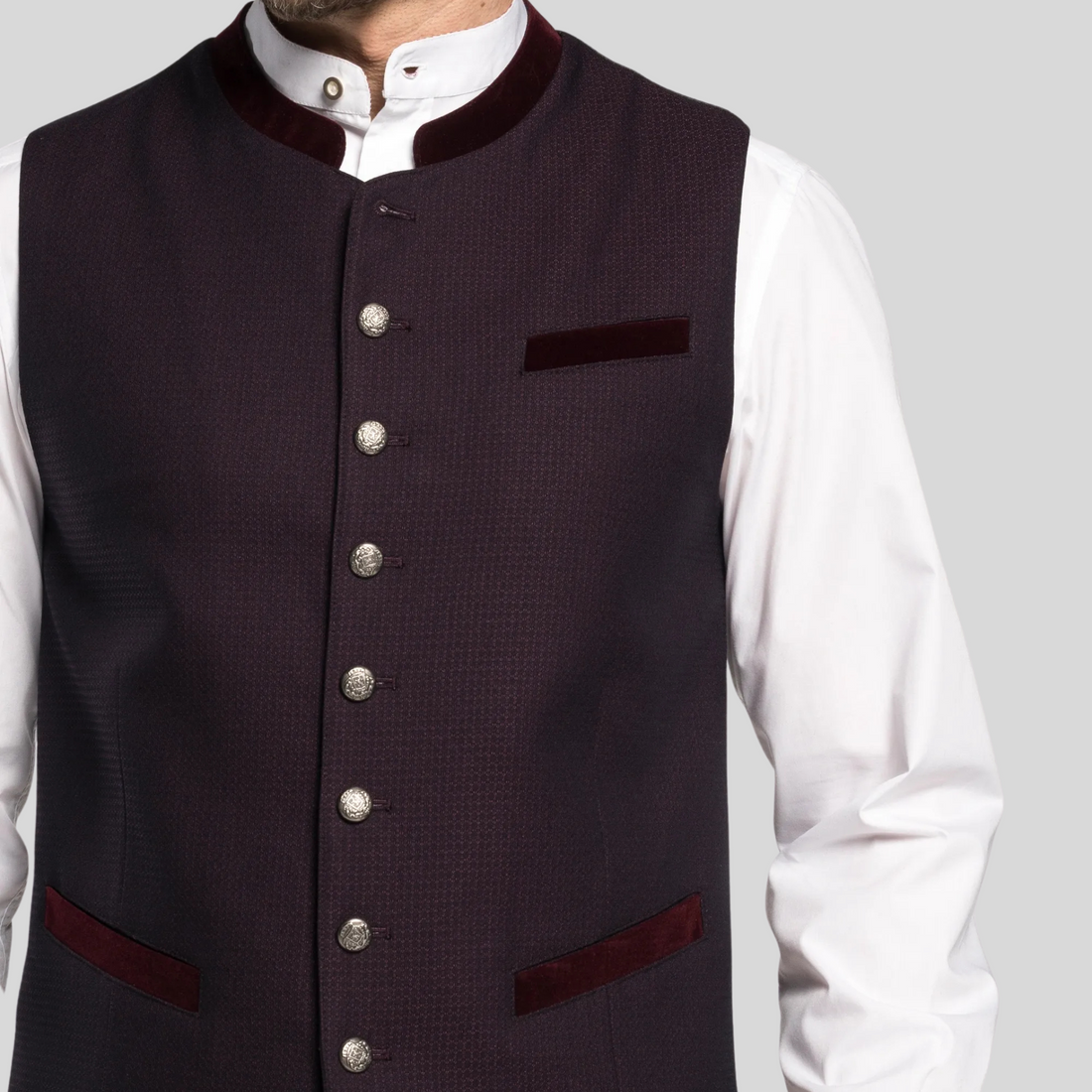 Man wearing a dark vest over a white shirt with beige pants on a gray background