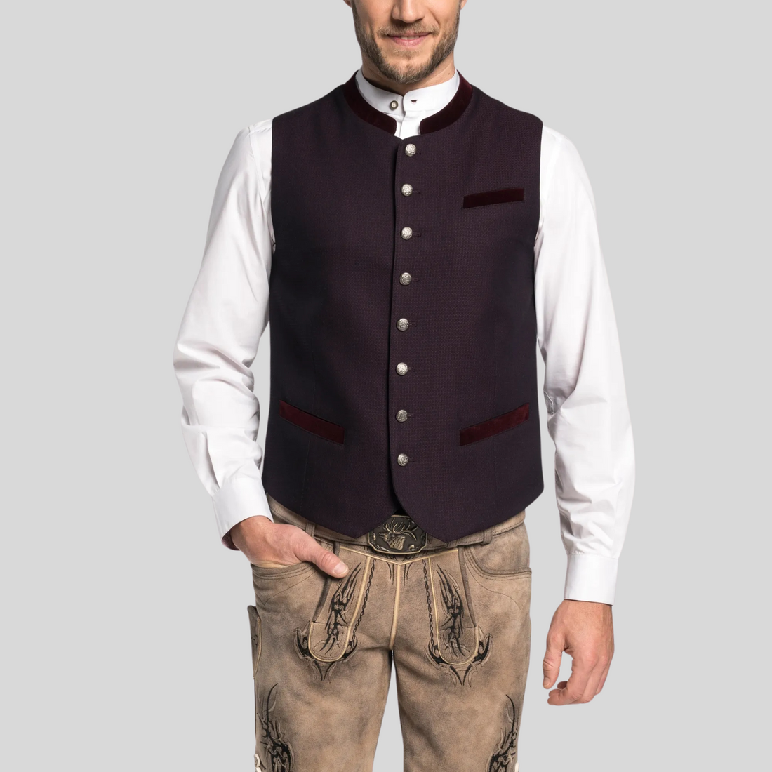 Man wearing a dark vest over a white shirt with beige pants on a gray background