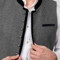 Close-up of a gray wool vest with black velvet trim and silver buttons, worn over a white collared shirt and adjusted by hands.