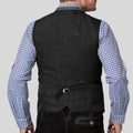 A man shown from the back wearing a black pinstriped waistcoat over a blue and white gingham check shirt, against a solid light gray background.