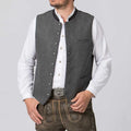 Man wearing a gray vest over a white shirt with brown pants on a light gray background