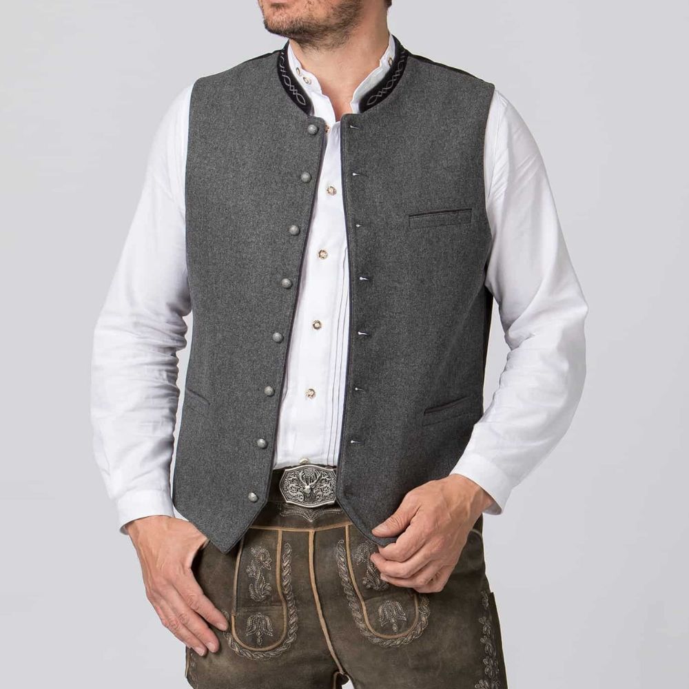 Man wearing a gray vest over a white shirt with brown pants on a light gray background
