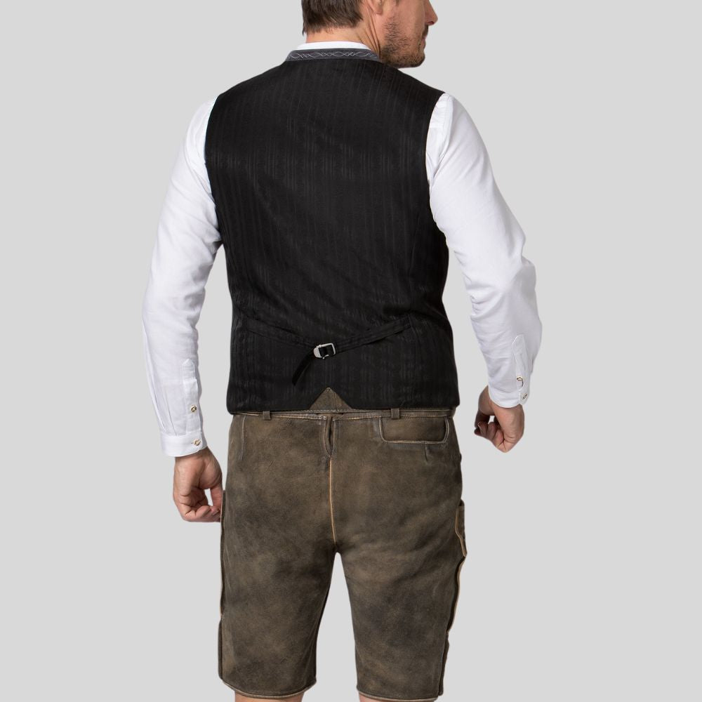 Man wearing a black vest over a white shirt with brown leather shorts on a light gray background