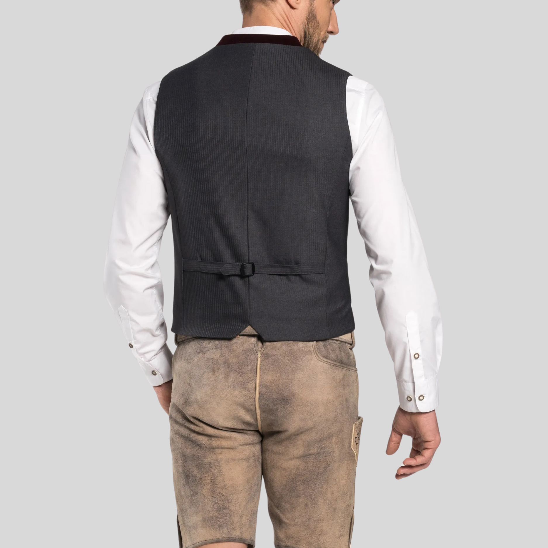 Man wearing a black vest over a white shirt with brown pants on a gray background